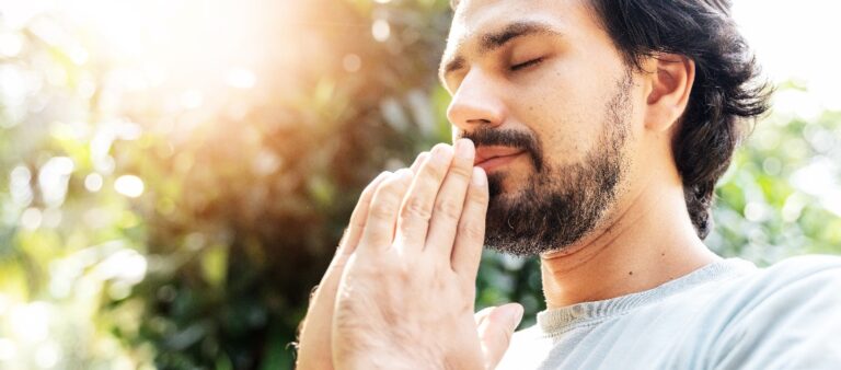 A bearded man is meditating outdoor in the park with face raised up to sky and eyes closed on sunny summer day concept of meditation dreaming wellbeing healthy lifestyle jpg