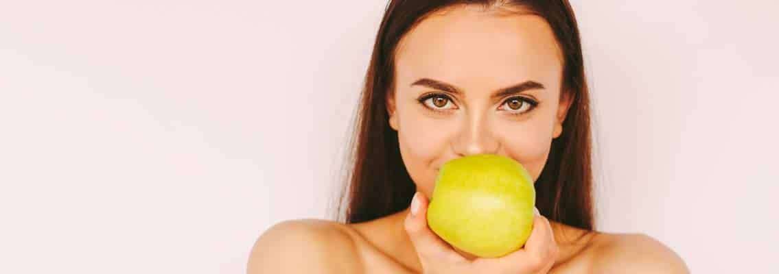 Lächelnde Frau mit Apfel als Symbol für Bleaching