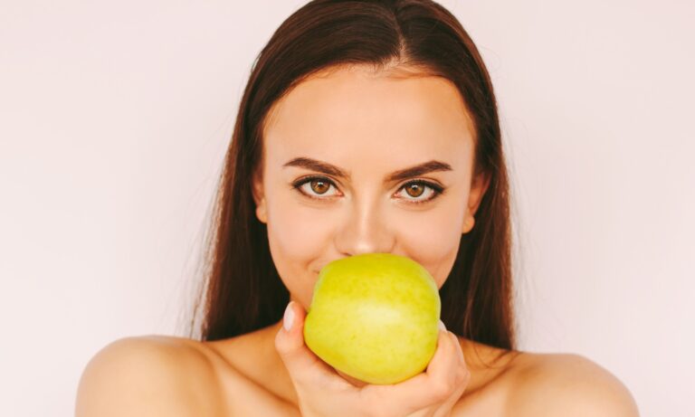 Lächelnde Frau mit Apfel als Symbol für Bleaching